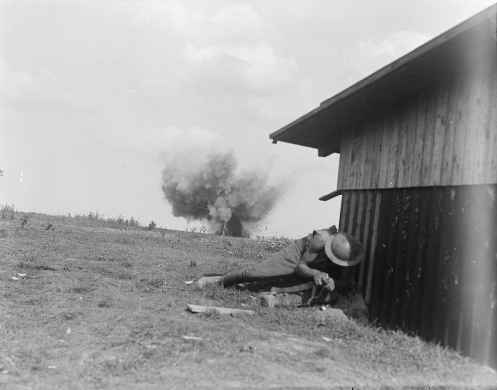 A New Zealand soldier takes cover as a German shell explodes behind him.